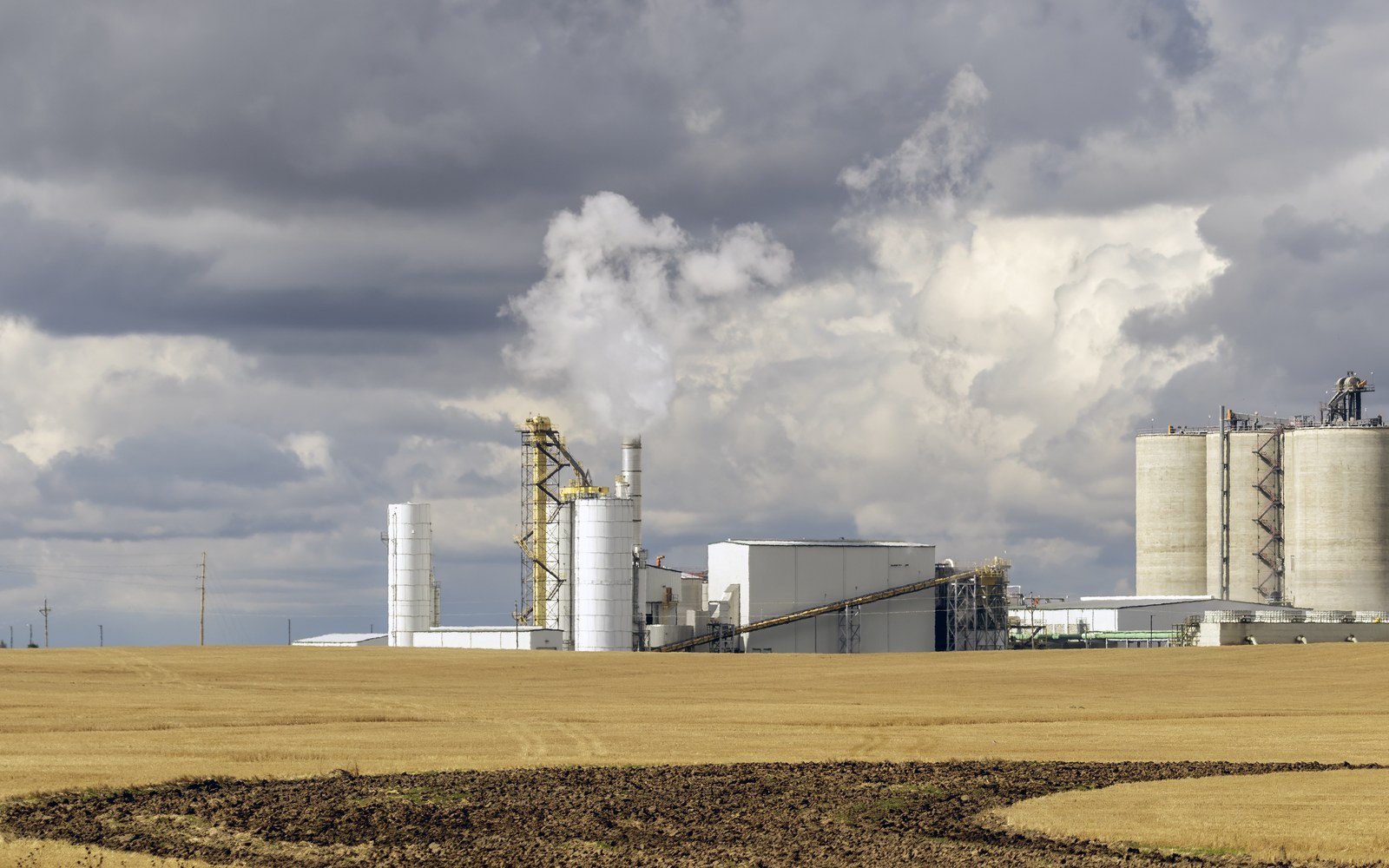 An ethanol plant with carbon capture equipment and a steam plume, seen across harvested farmland